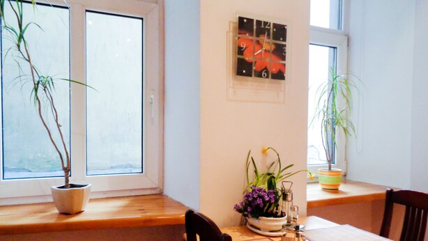 A dining area with a wooden table, chairs, a window with a view, and potted plants. - 1Br Apt In City Center by Minnehaha Lofts (Riga)