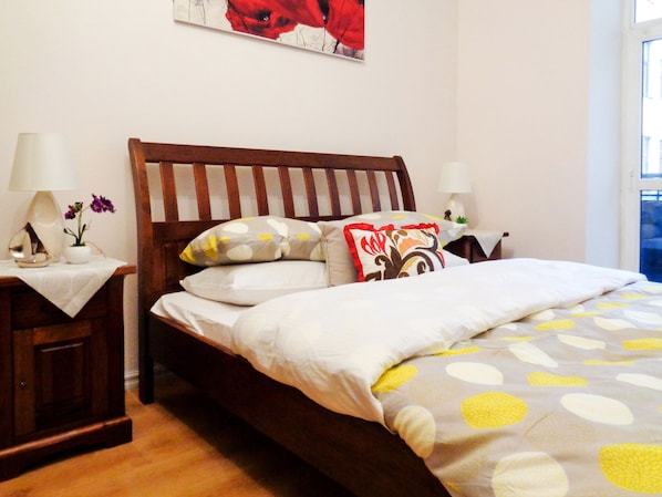 A neatly arranged bedroom with a wooden bed, white bedding, and a floral-patterned throw.