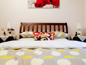 A neatly made bed with patterned bedding, a wooden headboard, and two bedside tables with lamps and decorative items.