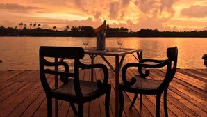 A wooden deck with two chairs and a table, overlooking a body of water with a sunset sky. - Malu Banna (Aluthgama)
