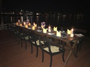 A long dining table set for a meal with chairs, candles, and a view of the water.