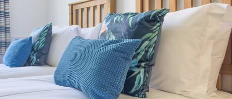 Cama con ropa de cama blanca, almohadas azules, cabecero de madera y un cuadro colgado en la pared.