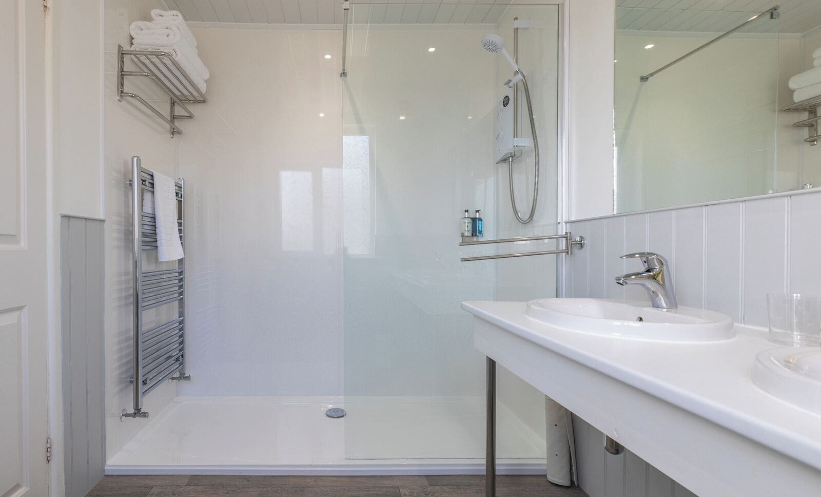 Une salle de bain moderne avec une douche à parois de verre, un lavabo blanc avec un miroir et un porte-serviettes.