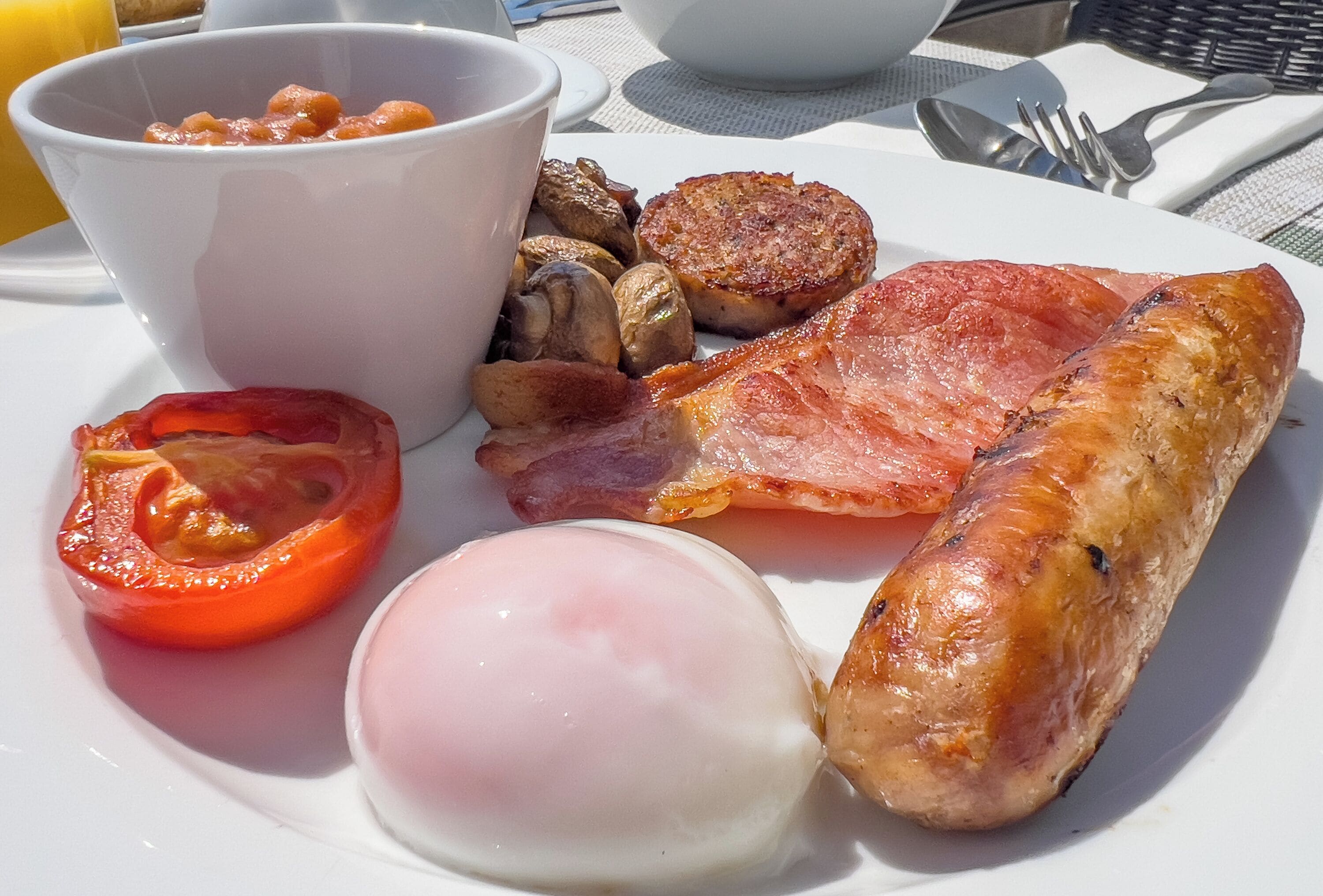 A breakfast plate with eggs, bacon, sausage, mushrooms, and a tomato.