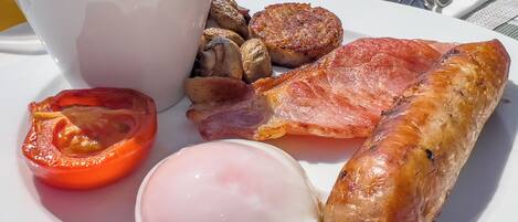 A breakfast plate with eggs, bacon, sausage, mushrooms, and a tomato.