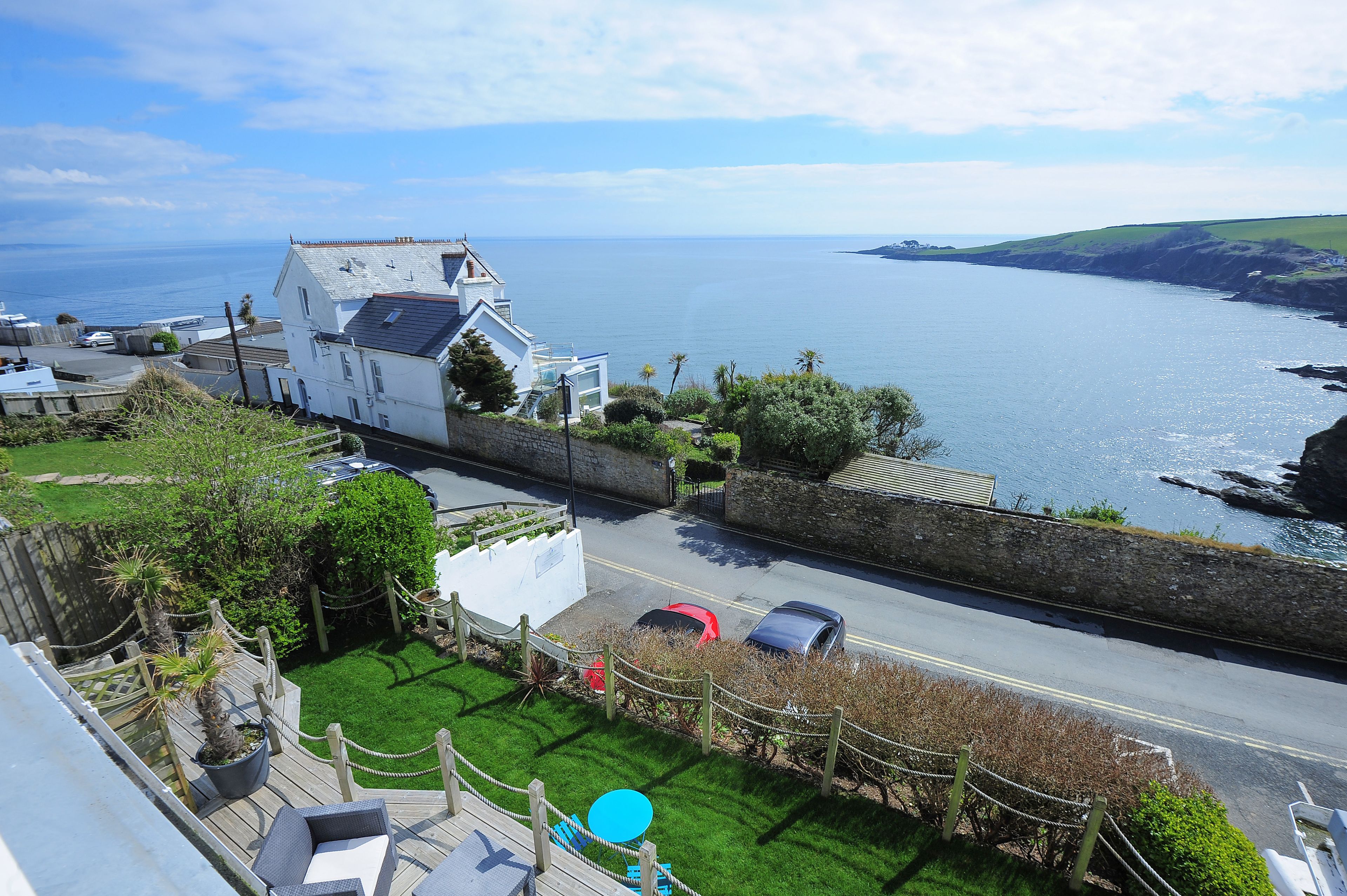 A coastal view with a white building, a paved road, and parked cars.