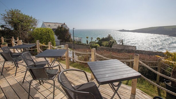 A wooden deck with tables and chairs overlooking a coastal view. - Mevagissey Bay Hotel (St Austell)