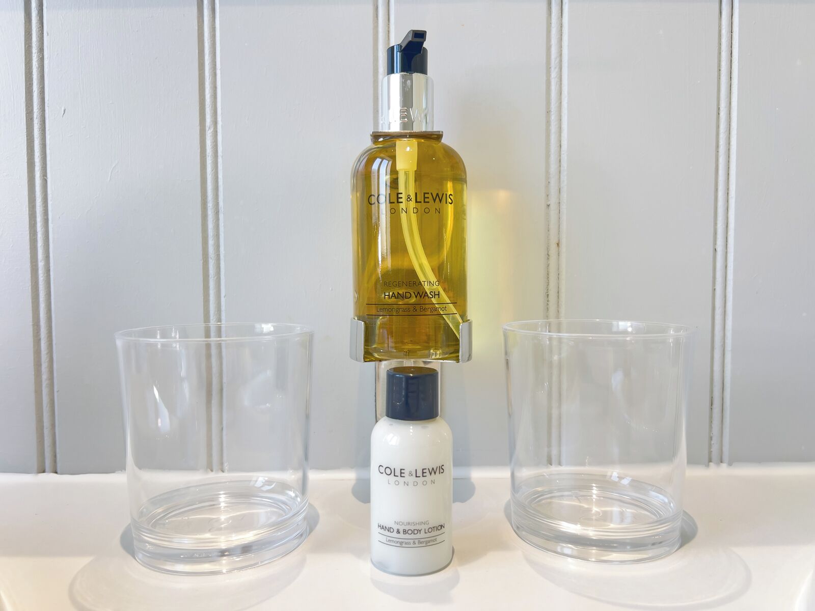 A bottle of hand wash and body lotion, a spray bottle, and two empty glass containers on a white surface.