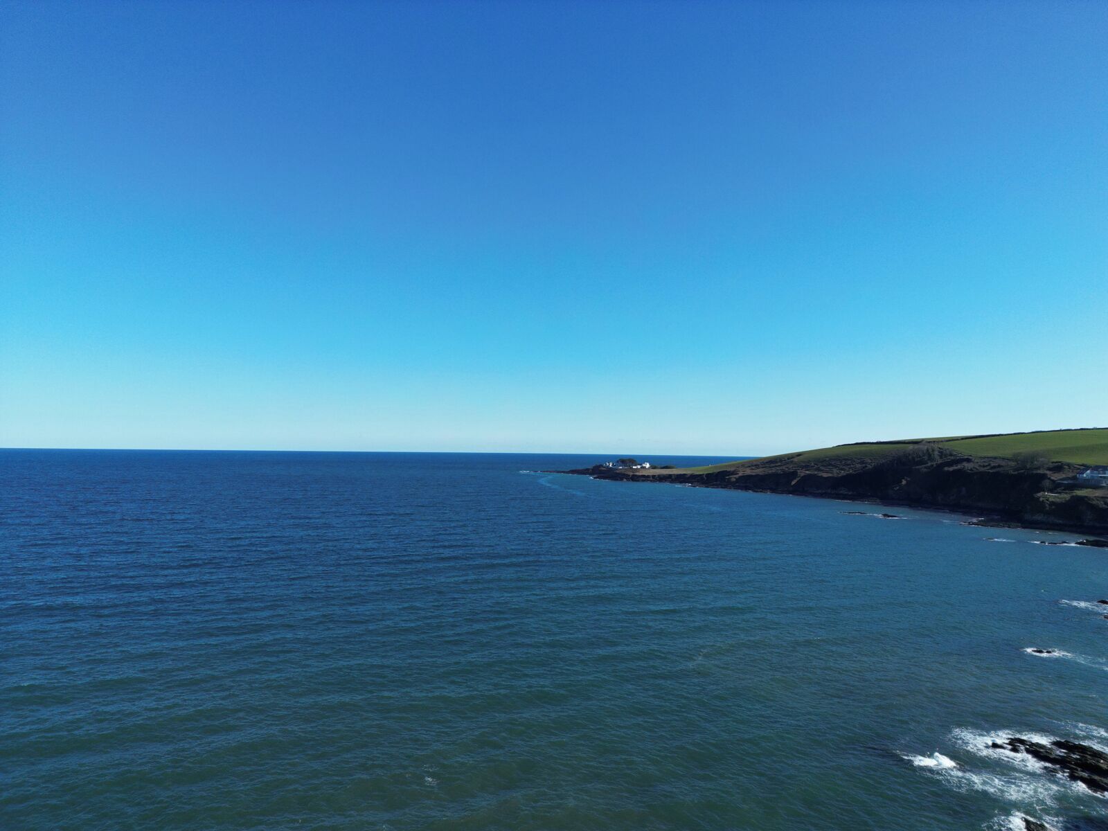 Un paisaje costero con cielo despejado, mar tranquilo y una colina cubierta de hierba.