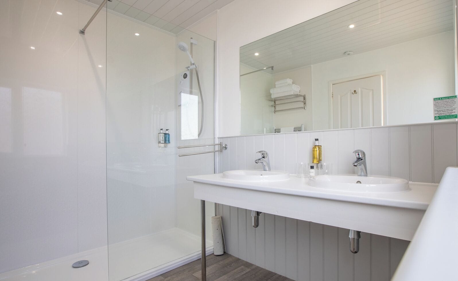 A modern bathroom with a glass-enclosed shower, two sinks, a large mirror, and a towel rack.