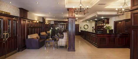 A spacious lobby with a bar area, seating arrangements, and a large chandelier.