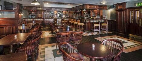 A bar area with wooden furniture, a checkered floor, and a bar counter with various bottles.