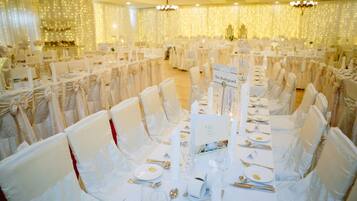A banquet hall with tables set for a formal event, featuring white tablecloths, chairs with bows, and a chandelier.