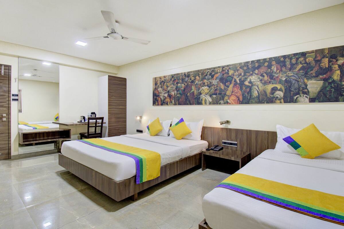 Quarto de hotel com duas camas, uma escrivaninha e um quadro grande na parede.