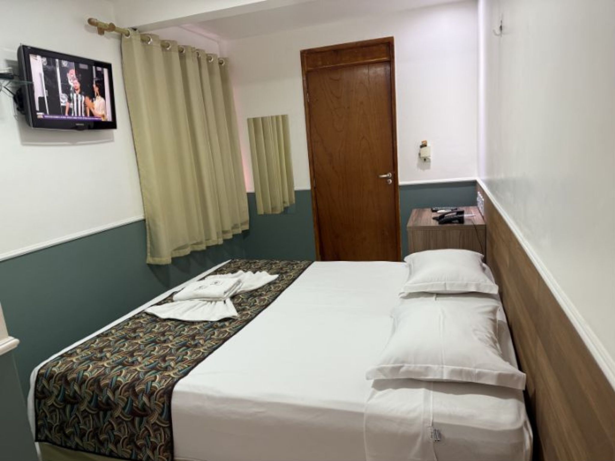 Una habitación de hotel con cama, cortinas, televisor y una puerta de madera.