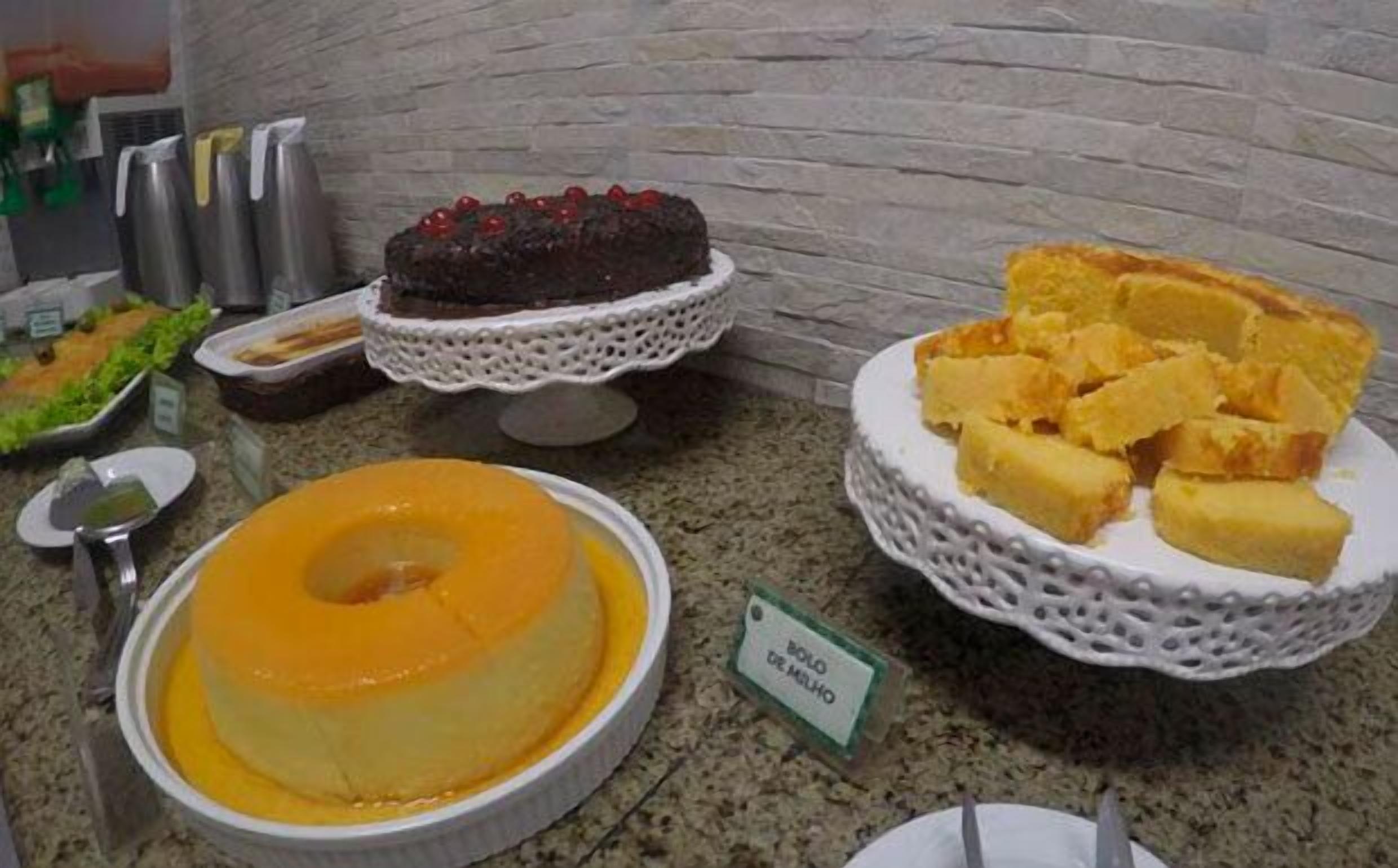 A buffet with various desserts including a chocolate cake, a yellow custard, and a plate of bread.