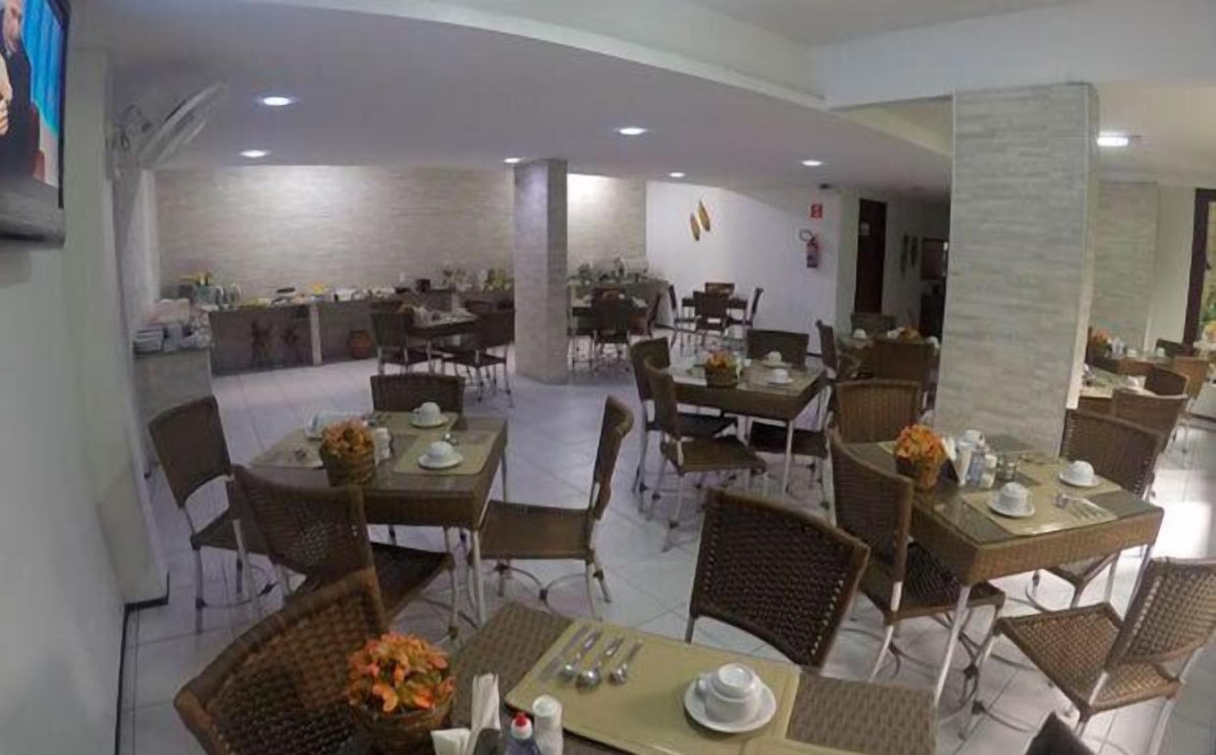 Un amplio comedor con múltiples mesas y sillas, un pilar central, y vistas de la sala contigua.