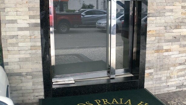 Entrada de hotel con puerta de vidrio, felpudo con el nombre del hotel y pared de ladrillo.