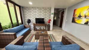 Una sala de estar con pared de ladrillo, televisor de pantalla plana, mobiliario de mimbre y un cuadro.