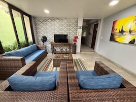 Una sala de estar con pared de ladrillo, televisor de pantalla plana, mobiliario de mimbre y un cuadro.