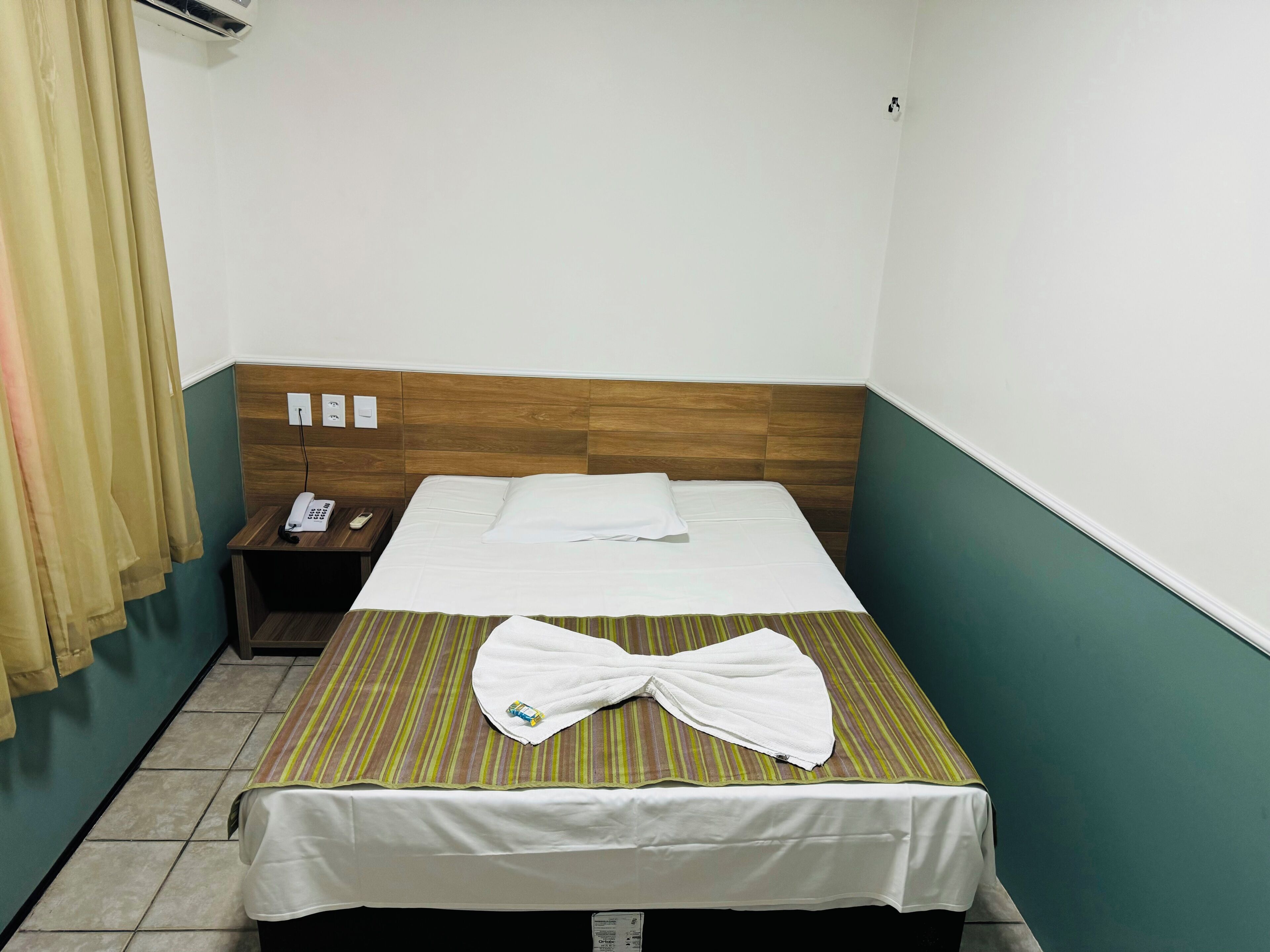 Habitación de hotel con cama, mesita de noche, teléfono y cortina.