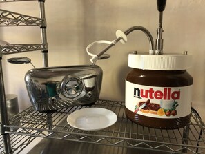 En köksdel med en brödrost och ett glas Nutella på en hylla av metall.