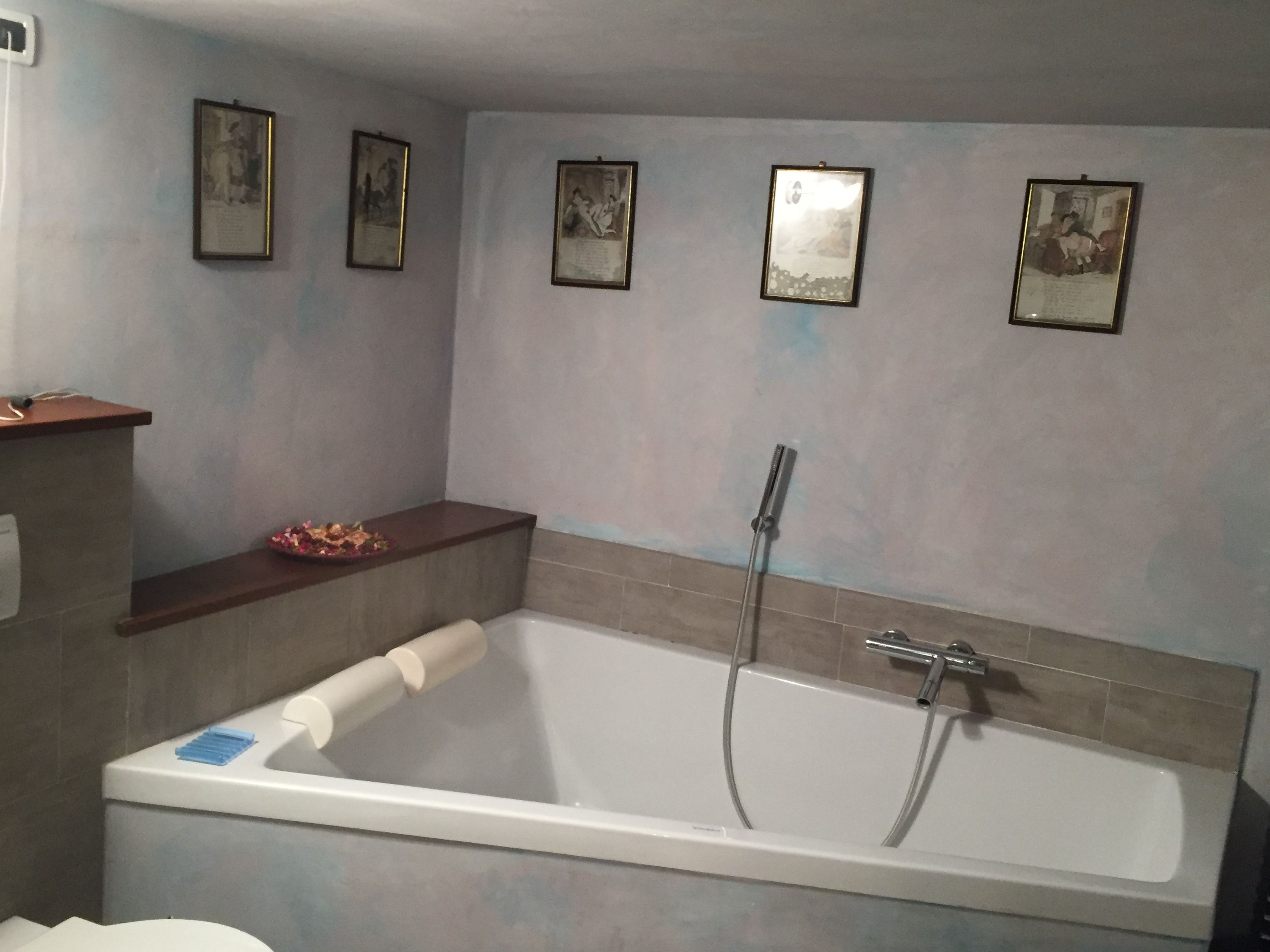 Un baño con bañera, ducha e inodoro. Hay cuadros enmarcados en la pared.