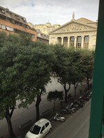 A street view with parked cars and trees lining the road.