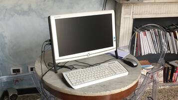 A desktop computer on a round table with a keyboard and mouse, surrounded by clear plastic chairs.