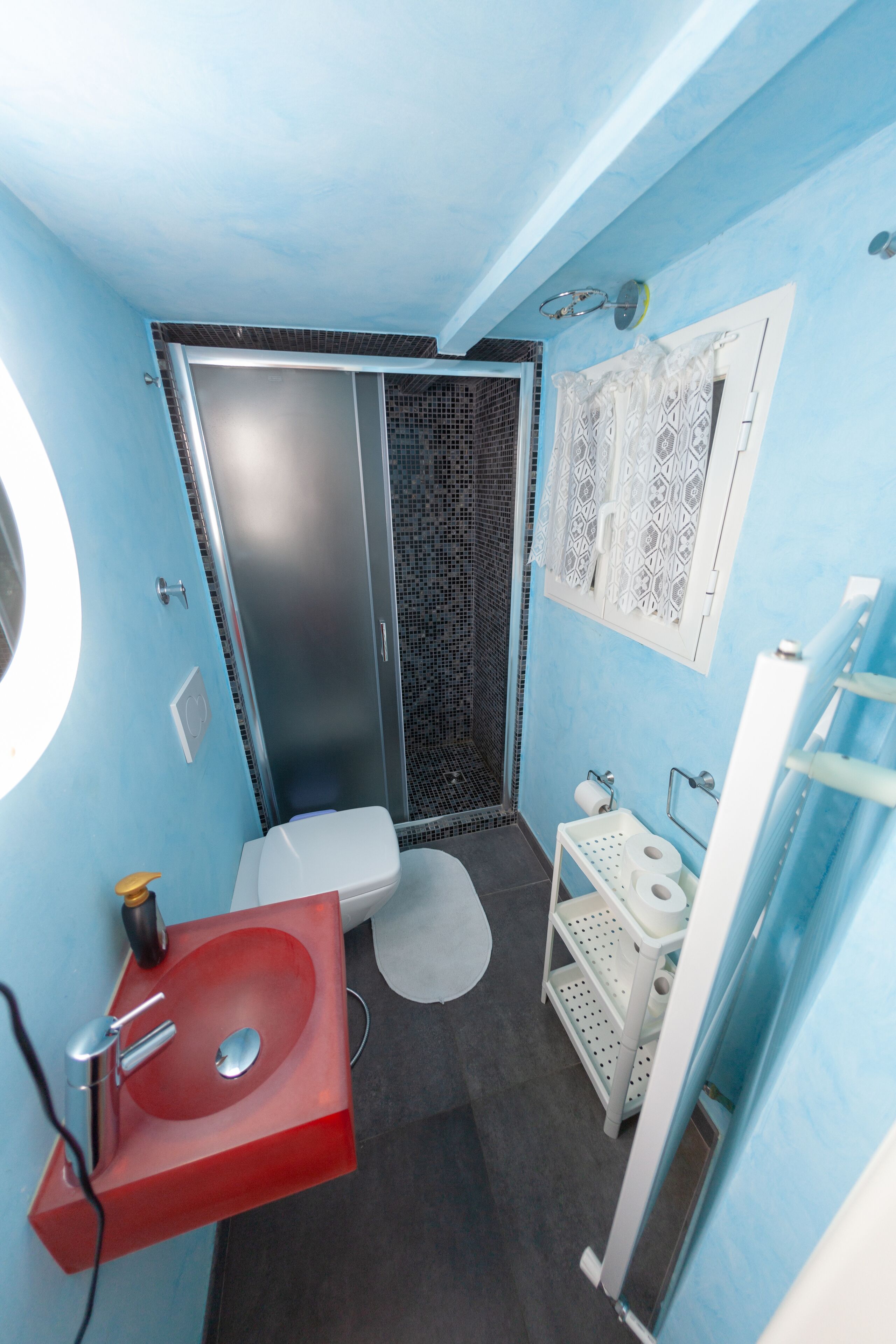 A compact bathroom with a red sink, a toilet, and a shower enclosure.