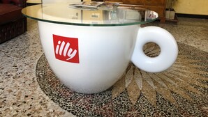 A large white mug with a handle, featuring a red logo, placed on a speckled tile floor.