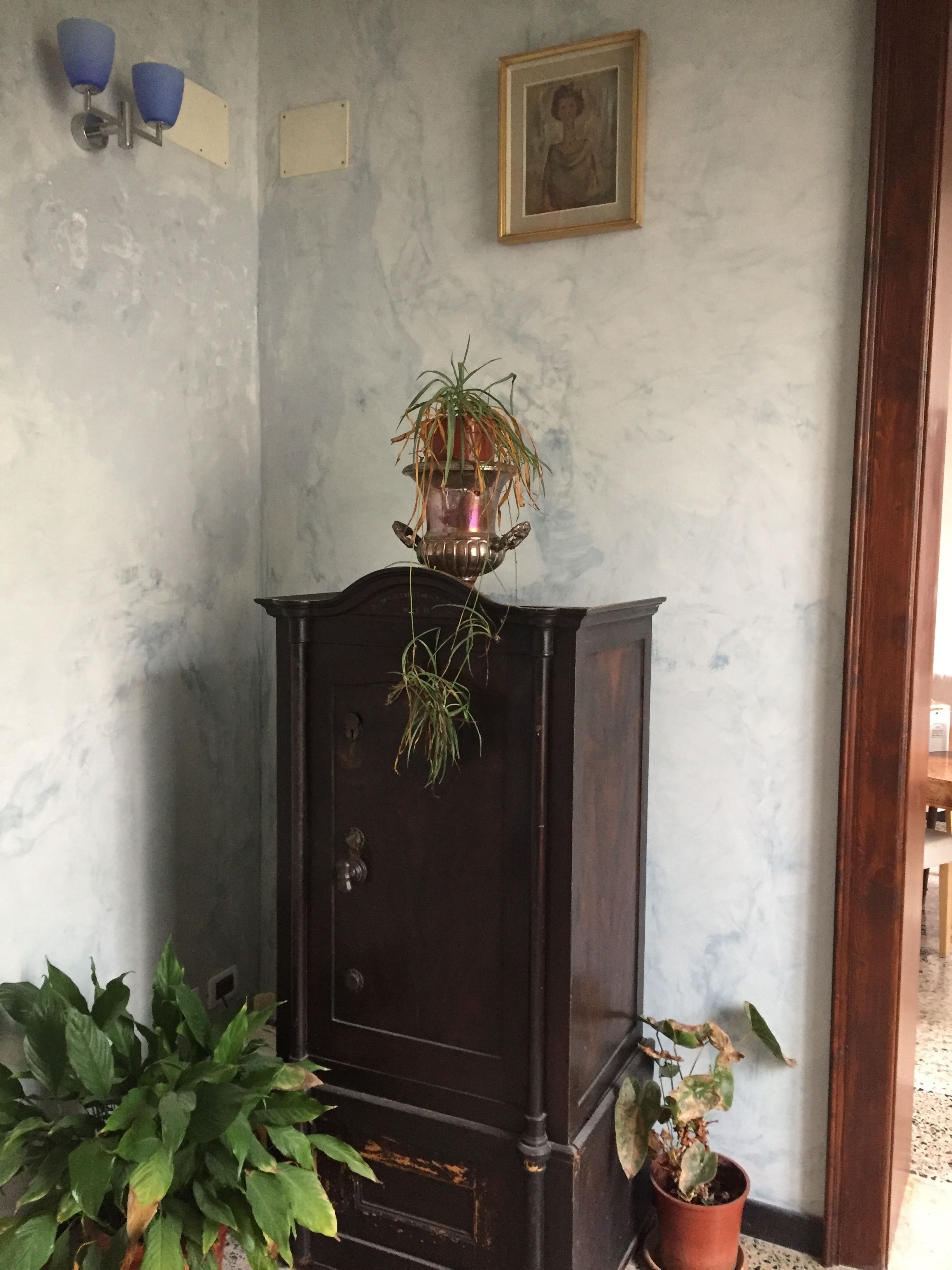 A corner room with a dark wooden cabinet, a potted plant on the floor, and a framed picture on the wall.