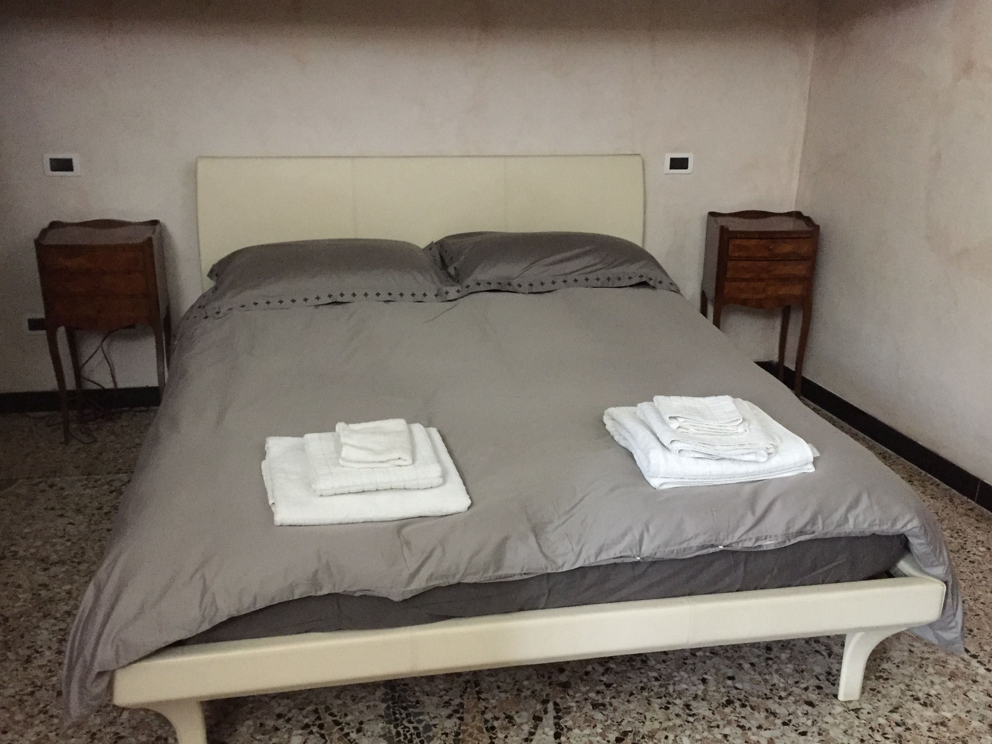 A neatly made bed with folded white towels, a grey bedspread, and matching pillows.