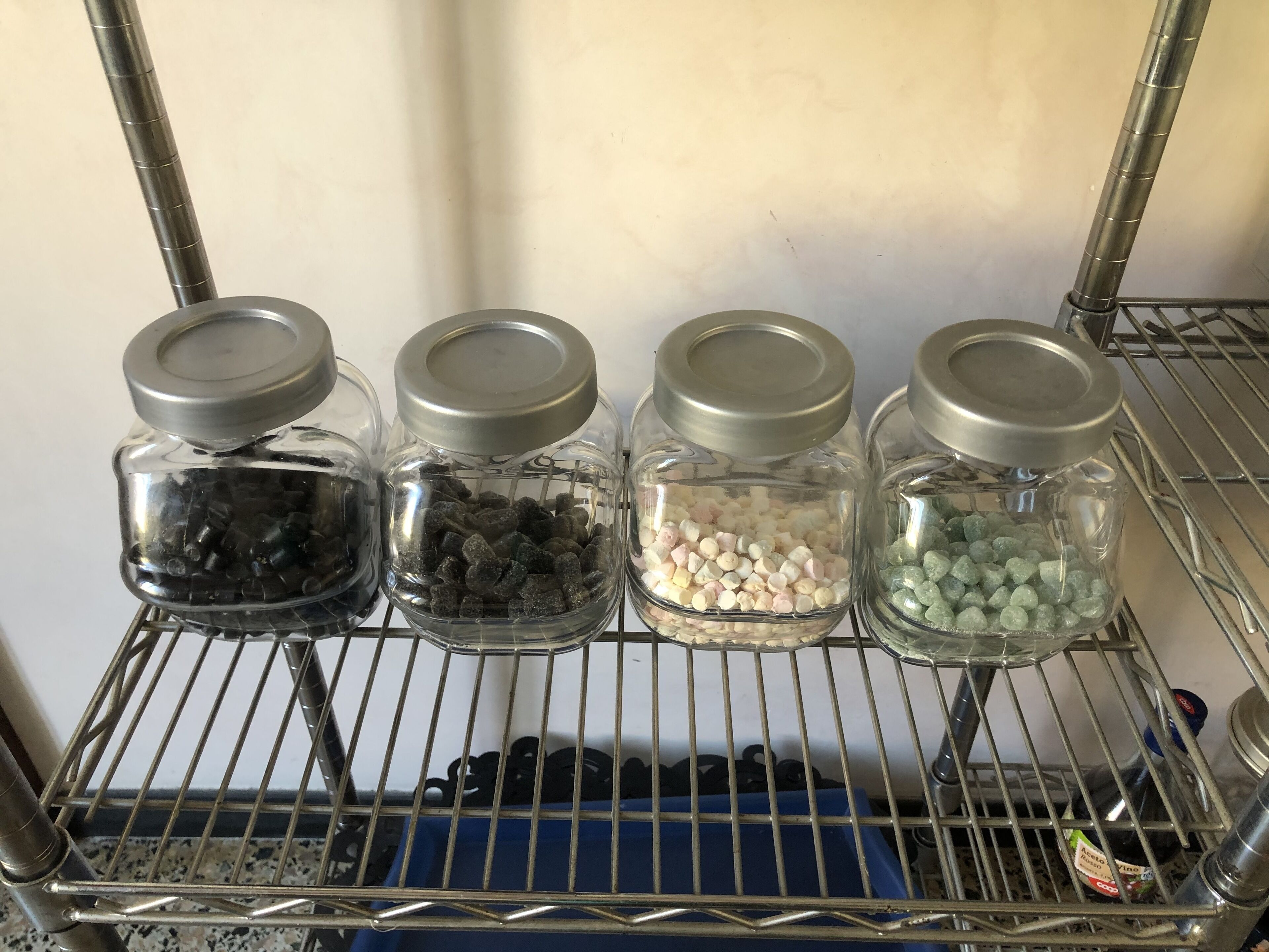 A metal shelf with four glass jars containing different colored candies.
