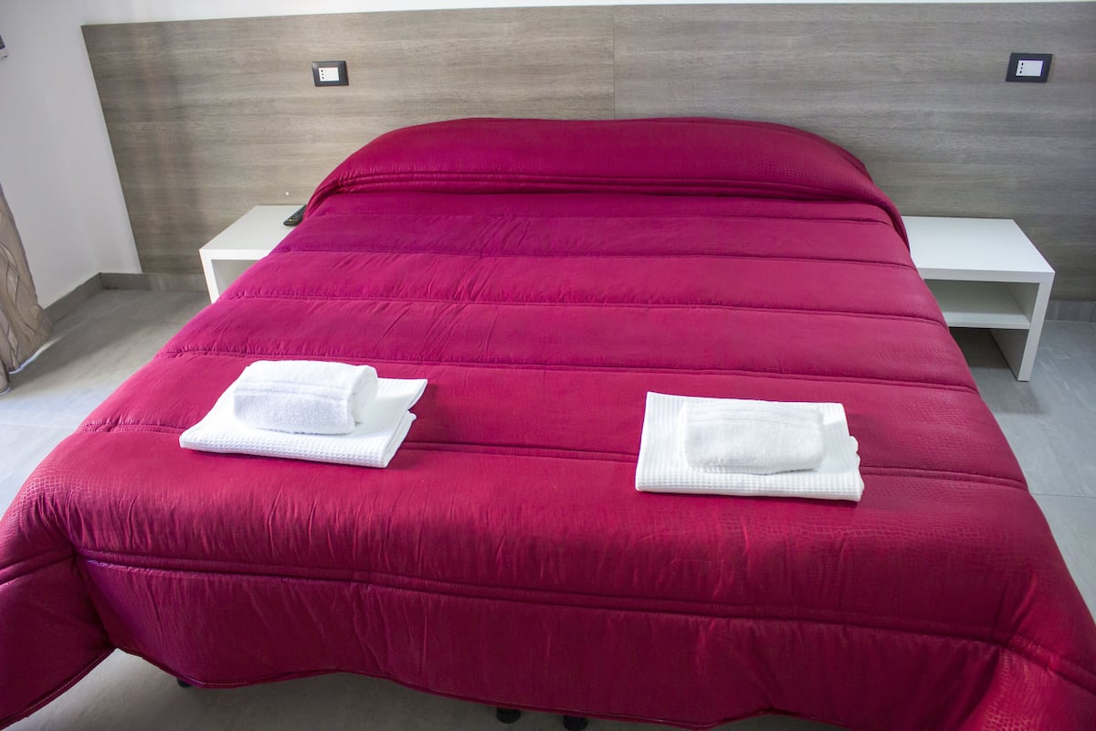 A bed with a red bedspread, two white towels, and a white nightstand.