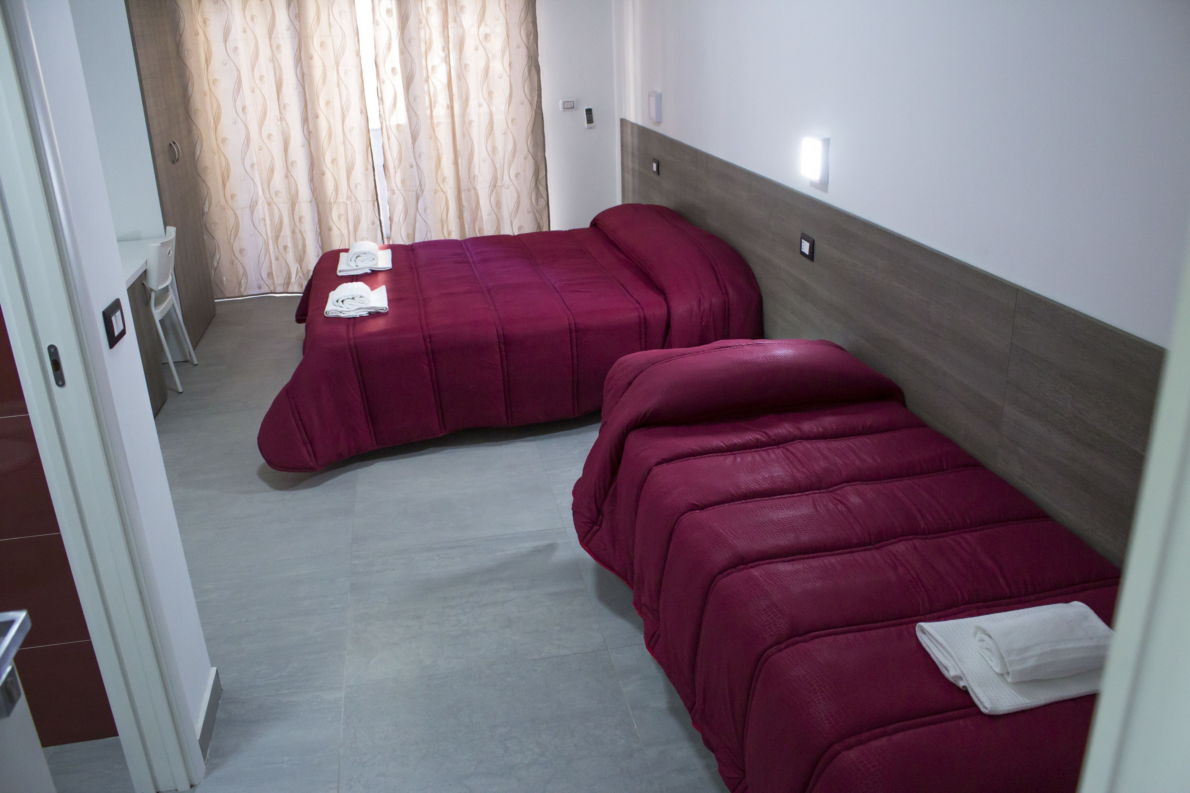 Quarto de hotel com duas camas, uma cadeira e uma pequena escrivaninha.