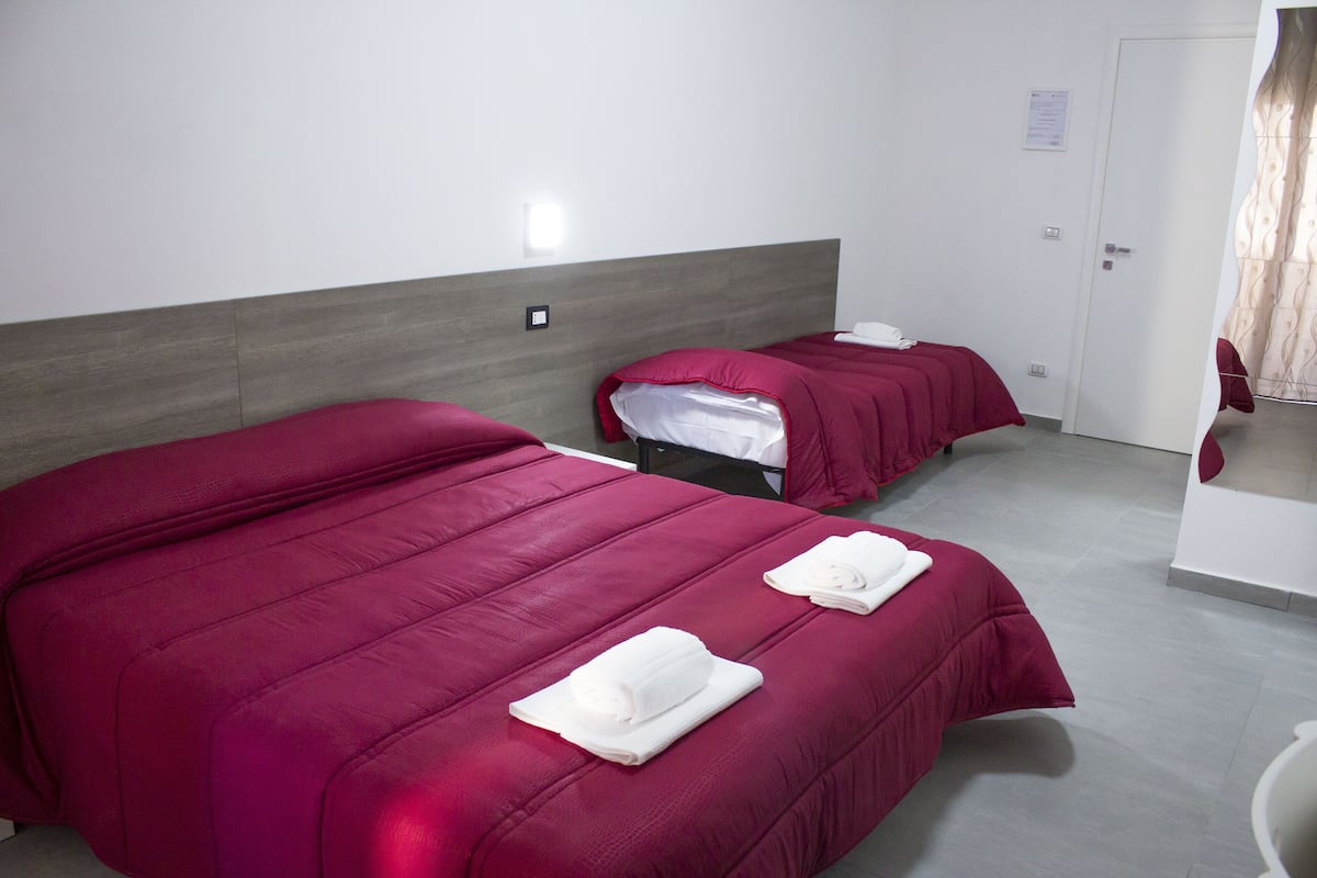 A hotel room with two beds, each with a red bedspread and white towels.
