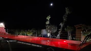 Vista nocturna de un estacionamiento con una barrera roja, un edificio con un letrero iluminado y un árbol.