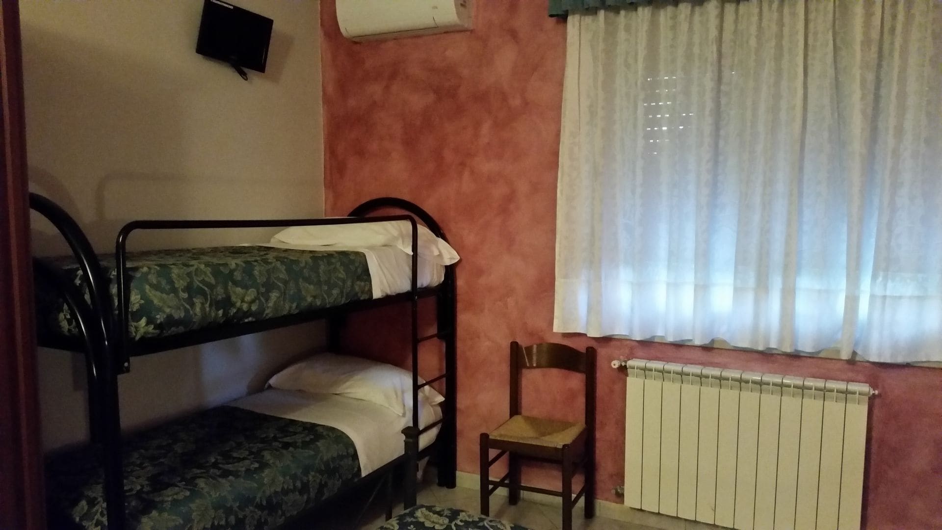 Ein Zimmer mit Etagenbetten, einem Heizkörper, einem Stuhl und einem Fenster mit Vorhängen.