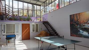 Ein geräumiges Zimmer mit einem Tischtennistisch, einem großen Fenster, einer Treppe und einem Gemälde.