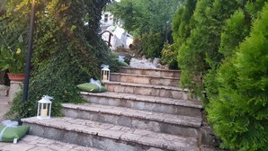 Una escalera de piedra con cojines verdes y faroles blancos, rodeada de abundante vegetación.