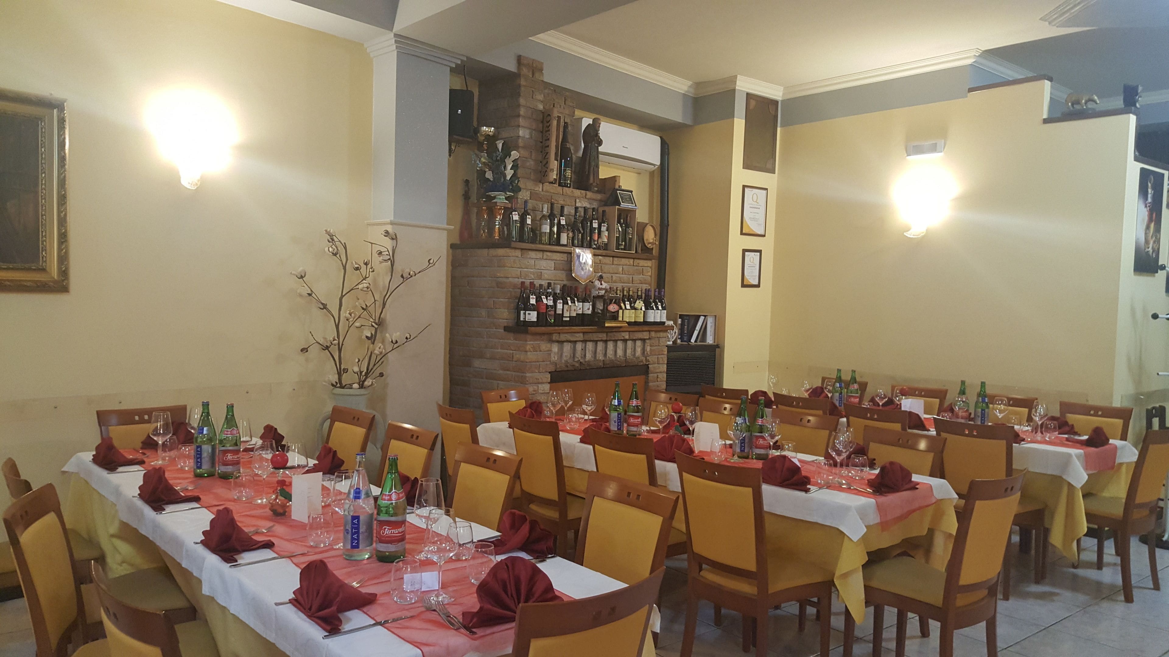 Un restaurante con varias mesas dispuestas para comer, una chimenea de ladrillo y una vitrina con vino.