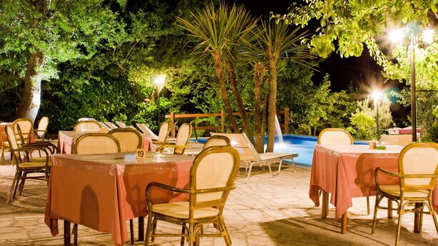 Un área de comedor al aire libre con mesas y sillas, rodeada de árboles y una piscina.