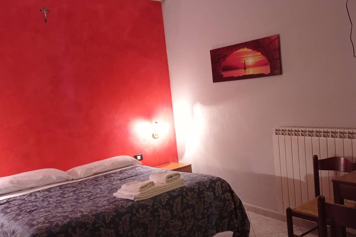 A hotel room with a red accent wall, a bed with a floral bedspread, a table with a vase of flowers, and a painting on the wall.