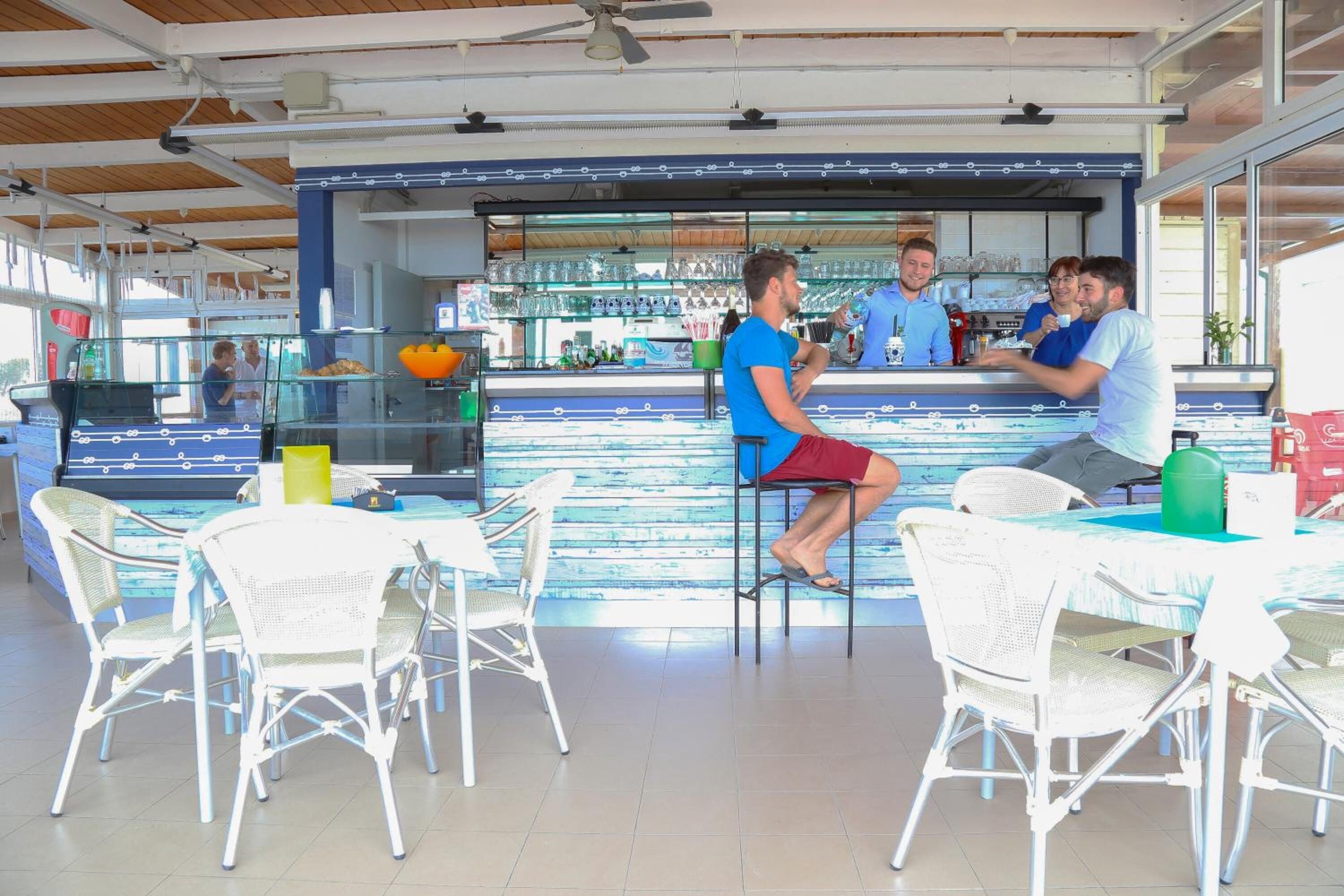 A bar area with white wicker chairs and a counter where staff are serving drinks.