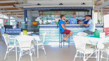 A bar area with white wicker chairs and a counter where staff are serving drinks.