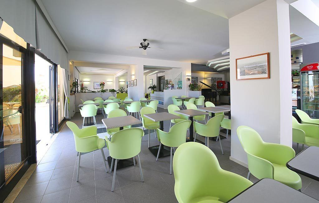 Un comedor moderno con sillas y mesas verdes, un ventilador de techo y vistas al exterior.