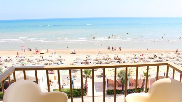 Vista a la playa desde un balcón con tumbonas y sombrillas.
