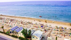 Una playa con numerosos sombrillas y sillas de playa, un pequeño edificio con el rótulo 'BACHI CARAVEL', y una vista despejada del mar.