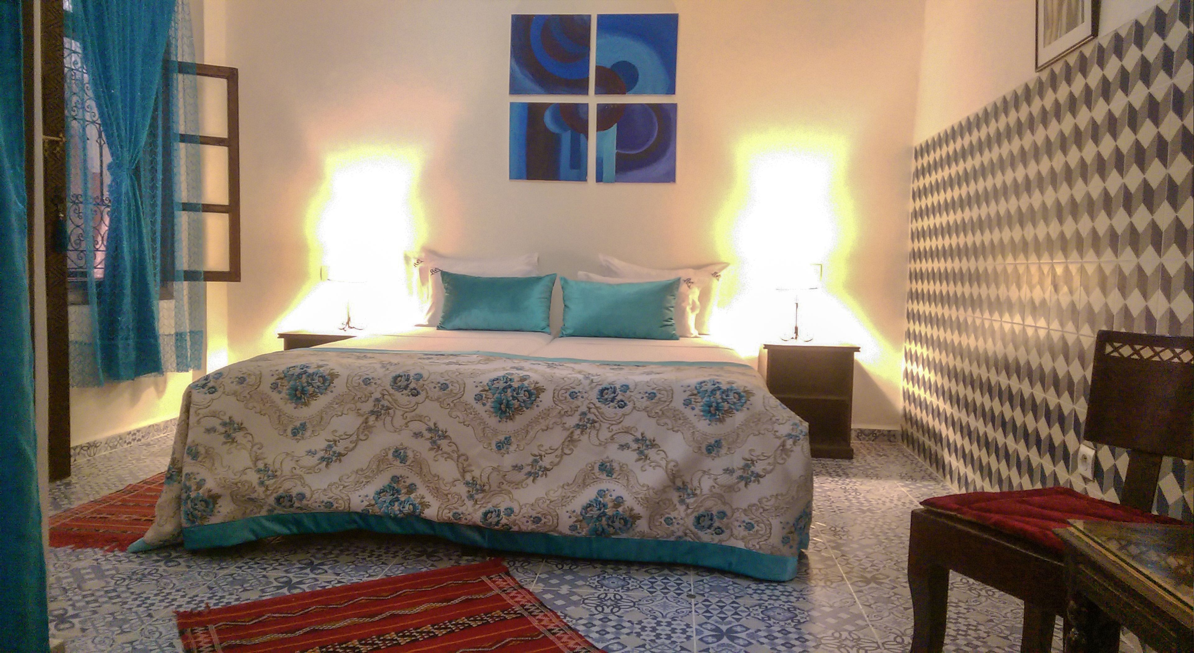 A bedroom with a bed, two bedside tables, a nightstand, a red rug, and patterned walls.